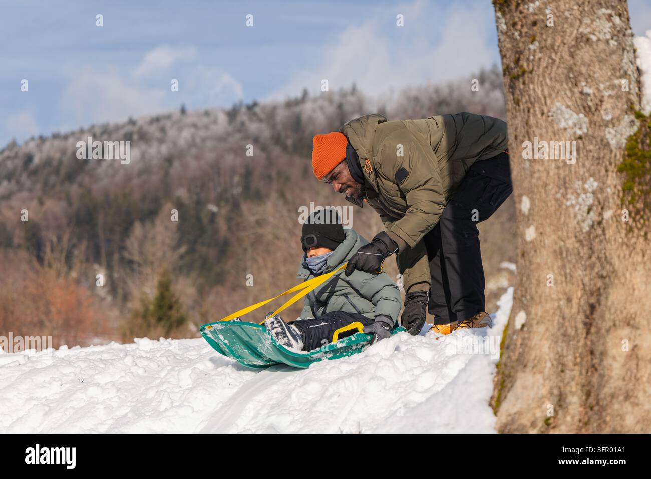 Un bambino si diverte a slittare con suo padre su una collina innevata, trascorrendo del tempo di qualità in famiglia e godendosi giochi invernali spensierati. Foto Stock