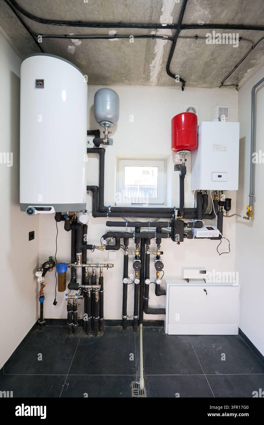 Sistema di riscaldamento con caldaia, serbatoi di espansione e rete di tubi installata nel ripostiglio. Configurazione moderna dell'impianto domestico con scaldabagno, pompe e idraulica, concetto di energia e manutenzione Foto Stock