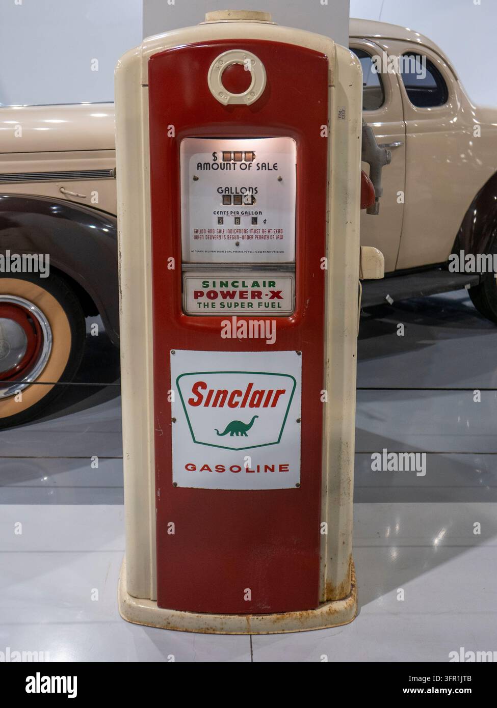 Pompa per benzina vintage rossa e crema Sinclair con logo di dinosauro e contatore meccanico del carburante esposta accanto ad un'auto classica antica. Foto Stock