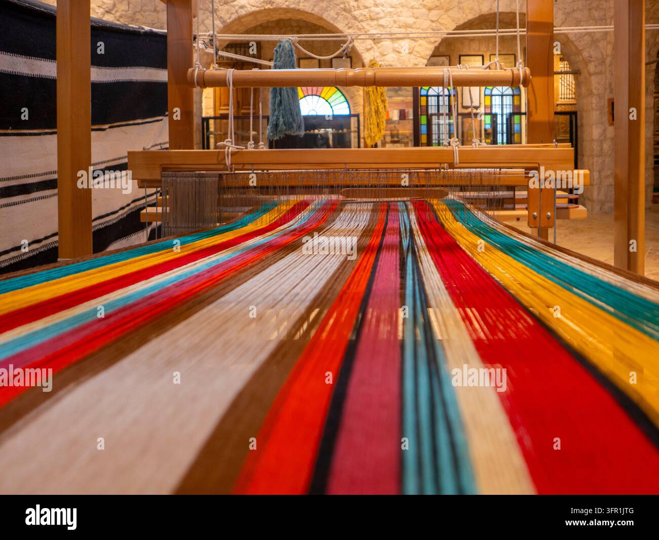 Tradizionale telaio in legno allestito con fili colorati, navetta e motivo artistico tessile geometrico vivace intrecciato in modo intricato. Foto Stock