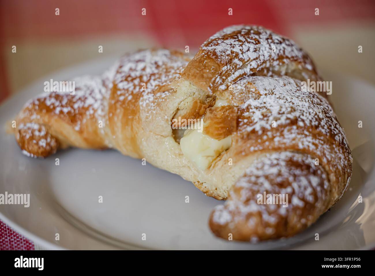 Croissant dolce appena sfornato, ripieno di crema alla vaniglia e spolverato di zucchero a velo su un piatto bianco Foto Stock