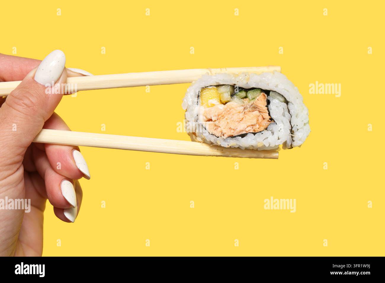 Rotolo di sushi al salmone tenuto con bacchette di legno su sfondo giallo. Cibo giapponese in primo piano per pranzo da asporto, frutti di mare e cucina asiatica. Foto Stock