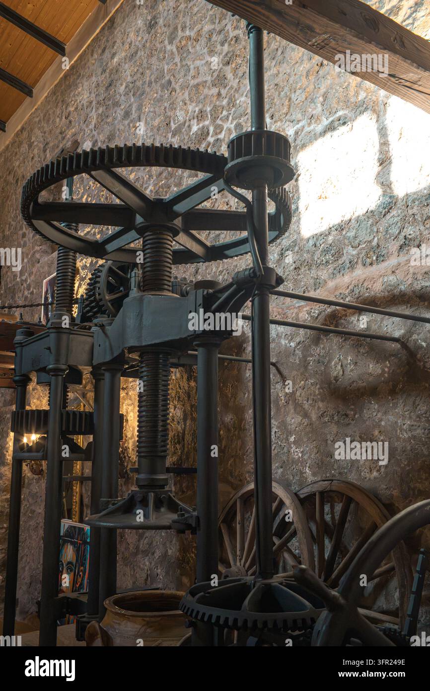 Un primo piano verticale di una vecchia pressa industriale con grandi ingranaggi, viti e meccanismi, forse per la produzione di olio d'oliva o vino. La macchina s Foto Stock