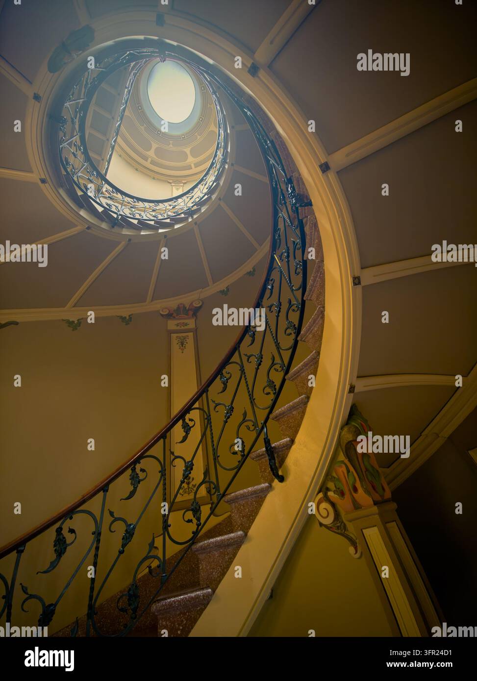 Una vista a bassa angolazione di una scala a chiocciola elegante all'interno di un edificio storico, che sale verso una cupola circolare. La ringhiera in ferro battuto ornata Foto Stock