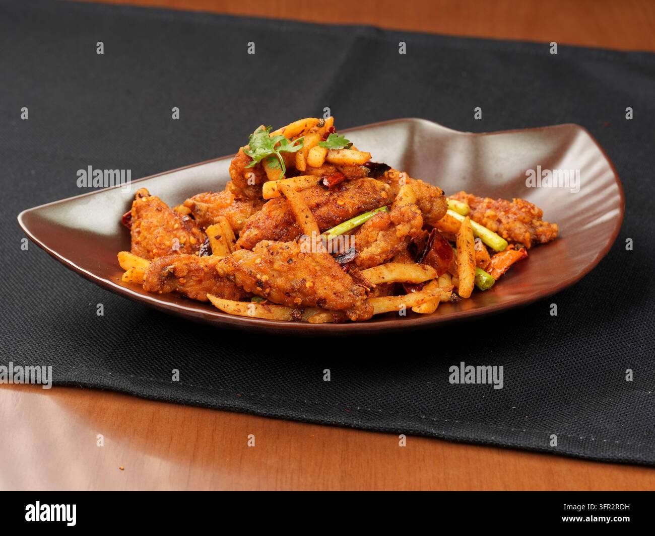 Alette di pollo fritte asciutte e strisce di patate con germogli d'aglio su piatto marrone Foto Stock