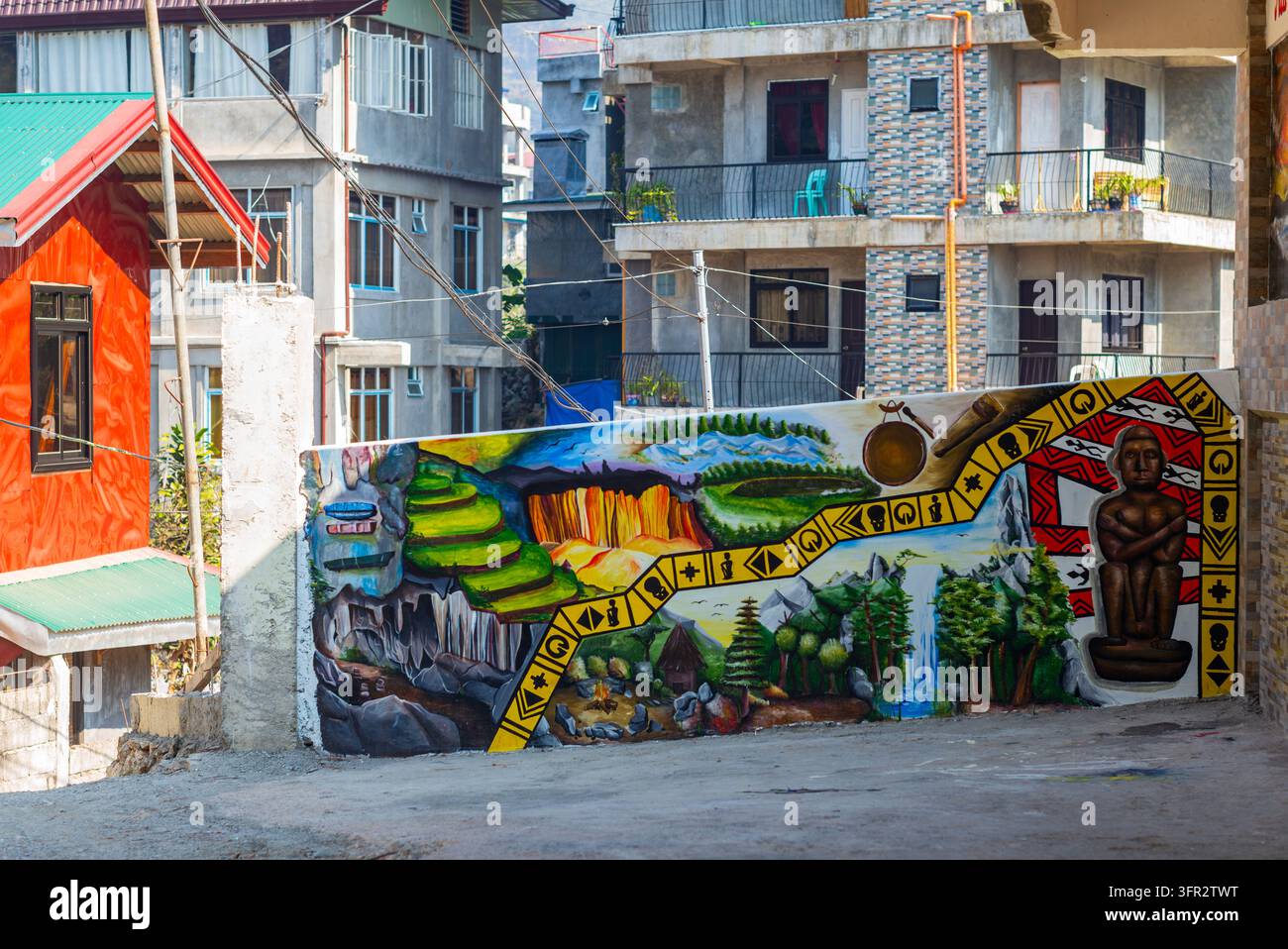 Un murale colorato con motivi paesaggistici e una figura umana stilizzata è dipinto su un muro stradale davanti ad edifici residenziali. Foto Stock