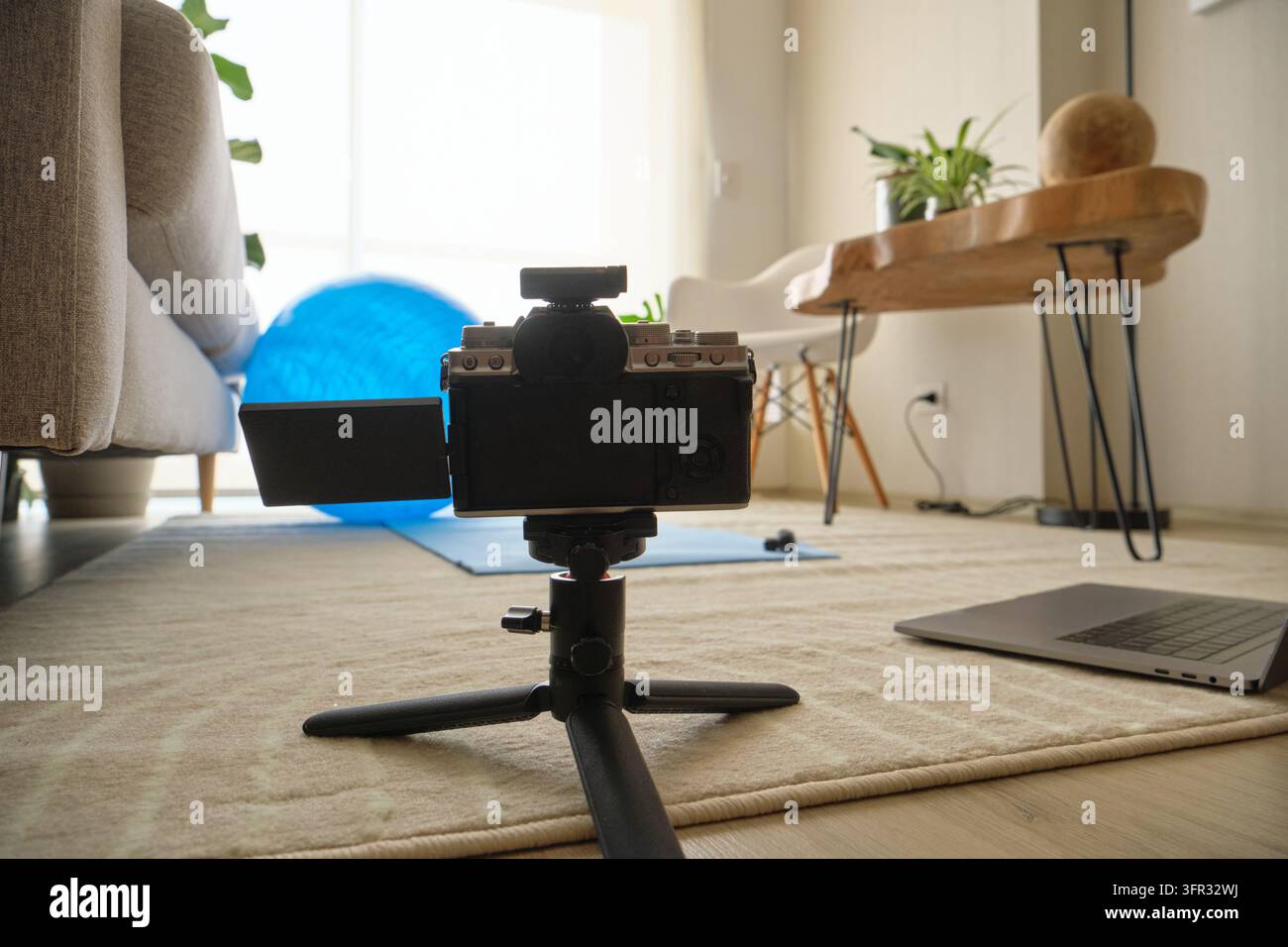 Fotocamera mirrorless su un treppiede che registra uno spazio di lavoro produttivo con laptop e tappetino da yoga Foto Stock