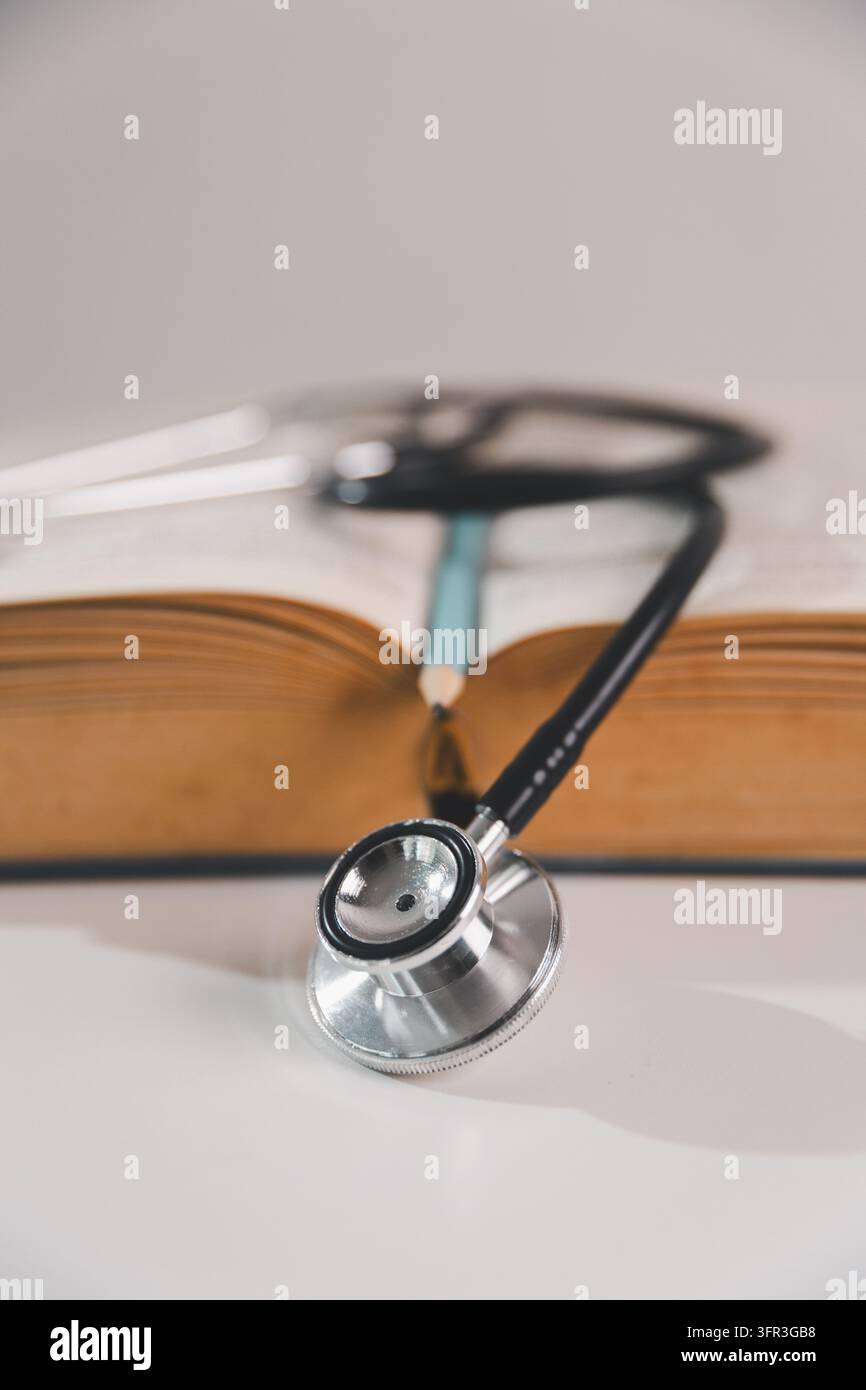 Stetoscopio posizionato davanti a un libro aperto con una matita, che rappresenta l'istruzione medica, l'apprendimento dell'assistenza sanitaria, lo studio accademico e la preparazione per un pro Foto Stock