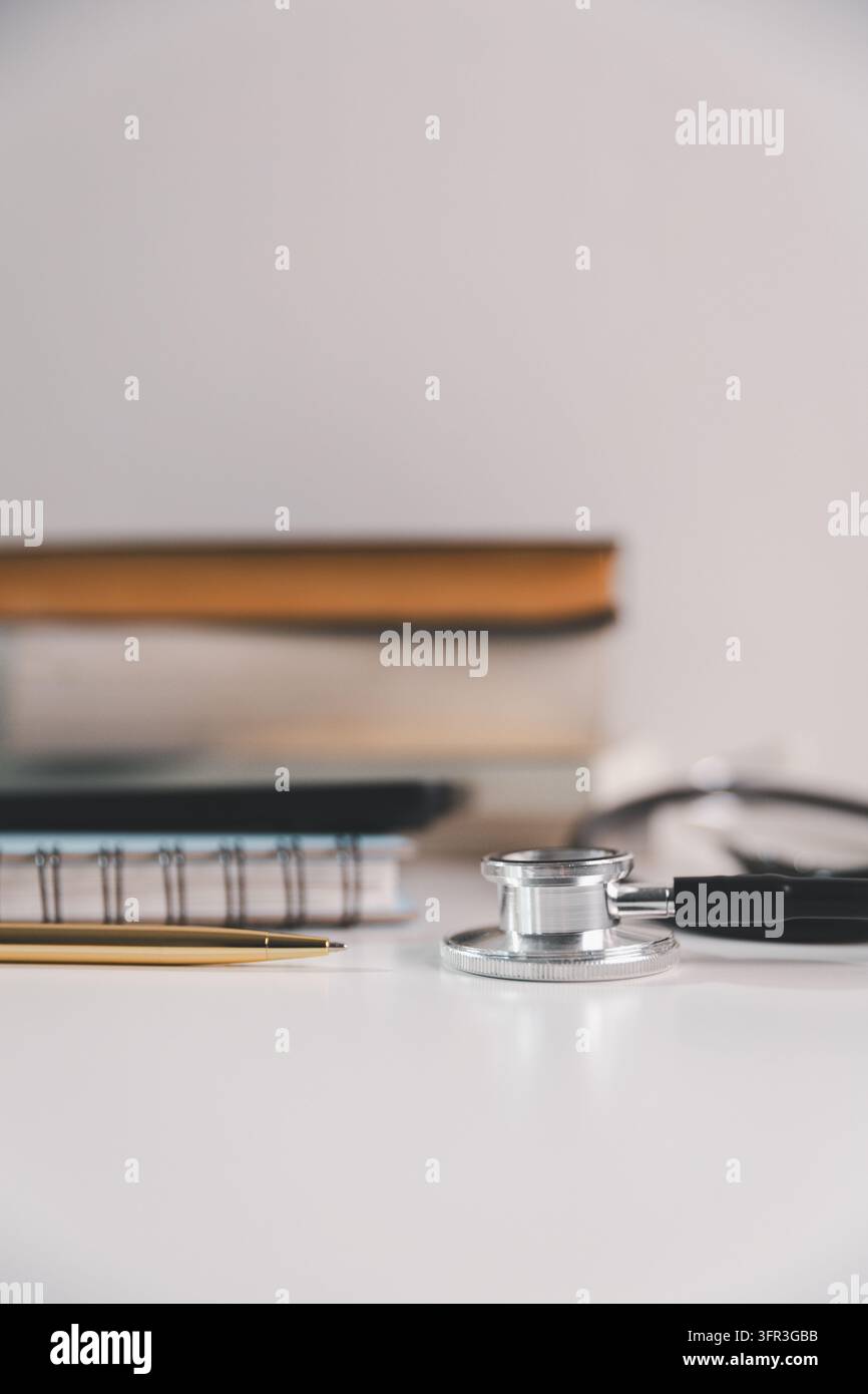 Stetoscopio, libri e penna su una scrivania pulita, simbolizzanti lo studio medico, l'apprendimento dell'assistenza sanitaria, la preparazione accademica e lo sviluppo professionale nel m Foto Stock