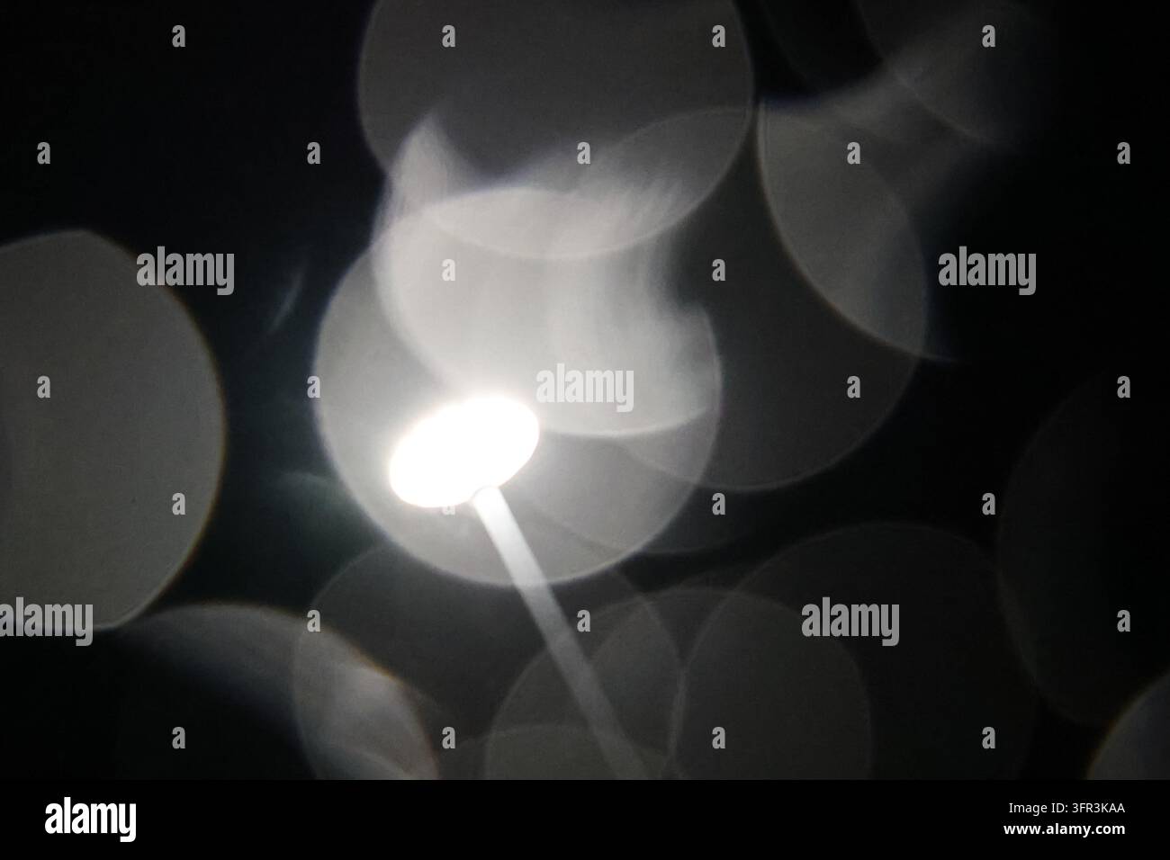 Lampione fotografato attraverso gocce di pioggia che creano grandi motivi circolari di bokeh di notte. Foto Stock