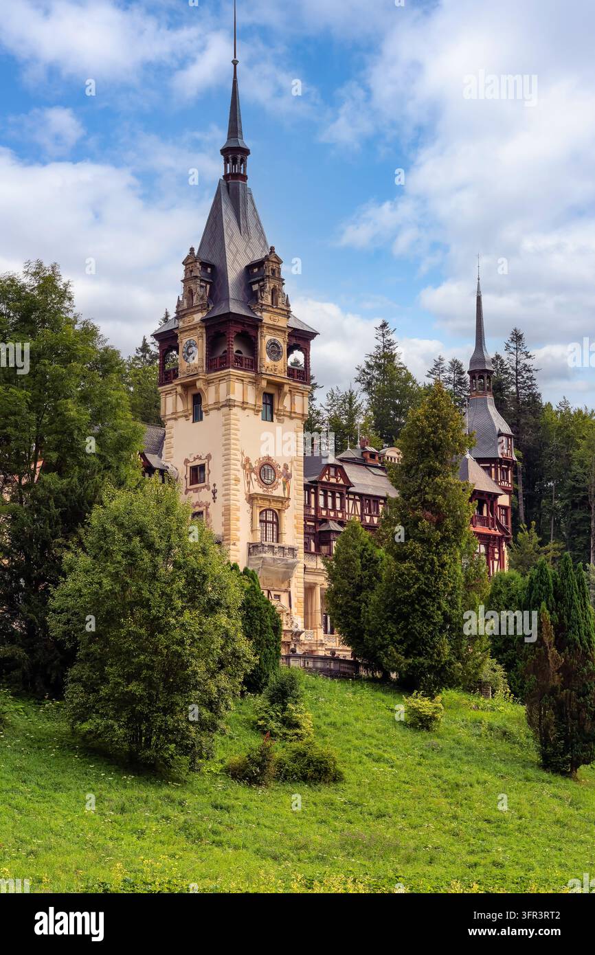 La torre dell'orologio del castello di Peles e le guglie appuntite ornate che si innalzano sopra gli alberi verdi a Sinaia, Romania Foto Stock