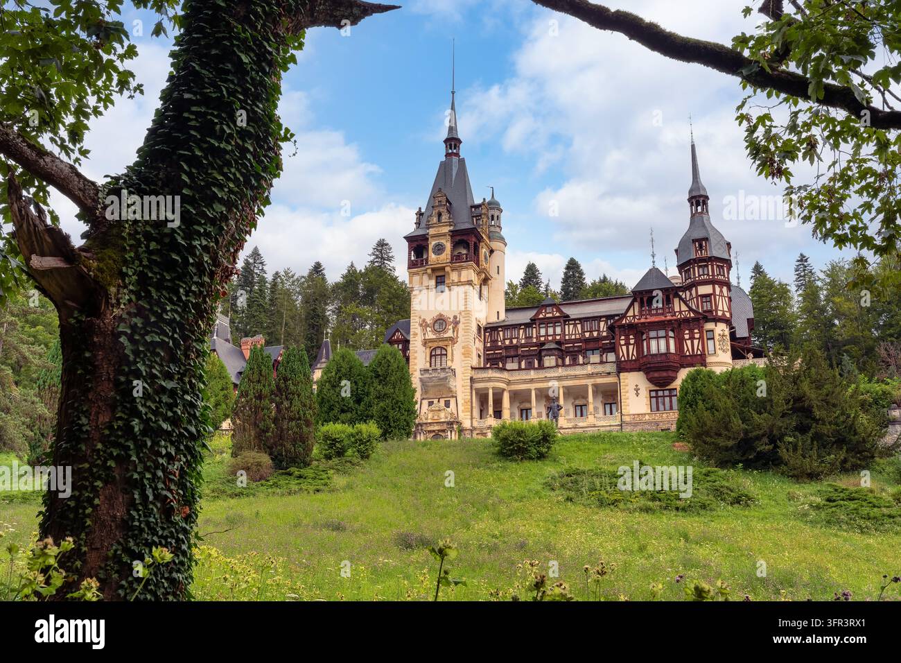 Il castello di Peles visto attraverso alberi frondosi con le sue torri ornate e la facciata storica a Sinaia, Romania Foto Stock