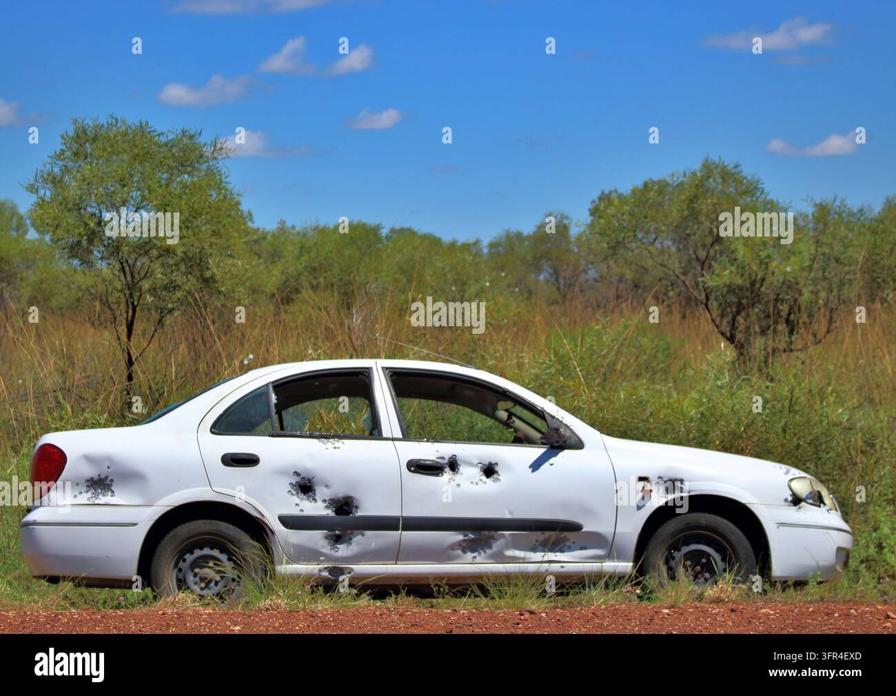 Una berlina bianca gravemente danneggiata con evidenti fori di proiettile e ammaccature è fermata nell'erba sul ciglio della strada nel Northern Territory, Australia. Foto Stock