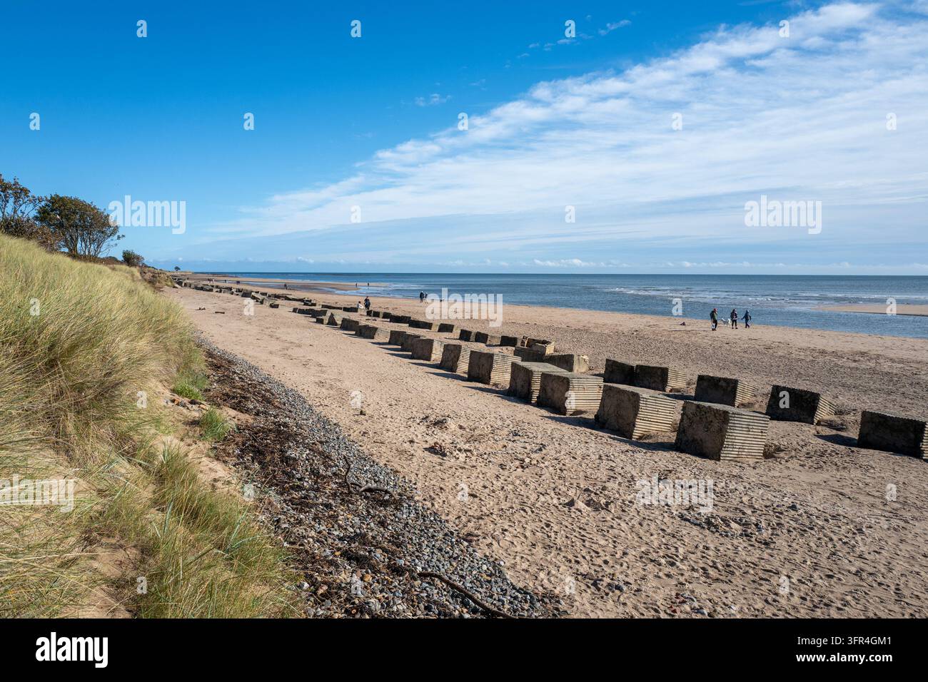 Un ampio paesaggio che mostra fortificazioni difensive storiche su una vasta linea costiera sotto un cielo blu luminoso nel villaggio costiero di Alnmouth, Northumberland. Foto Stock
