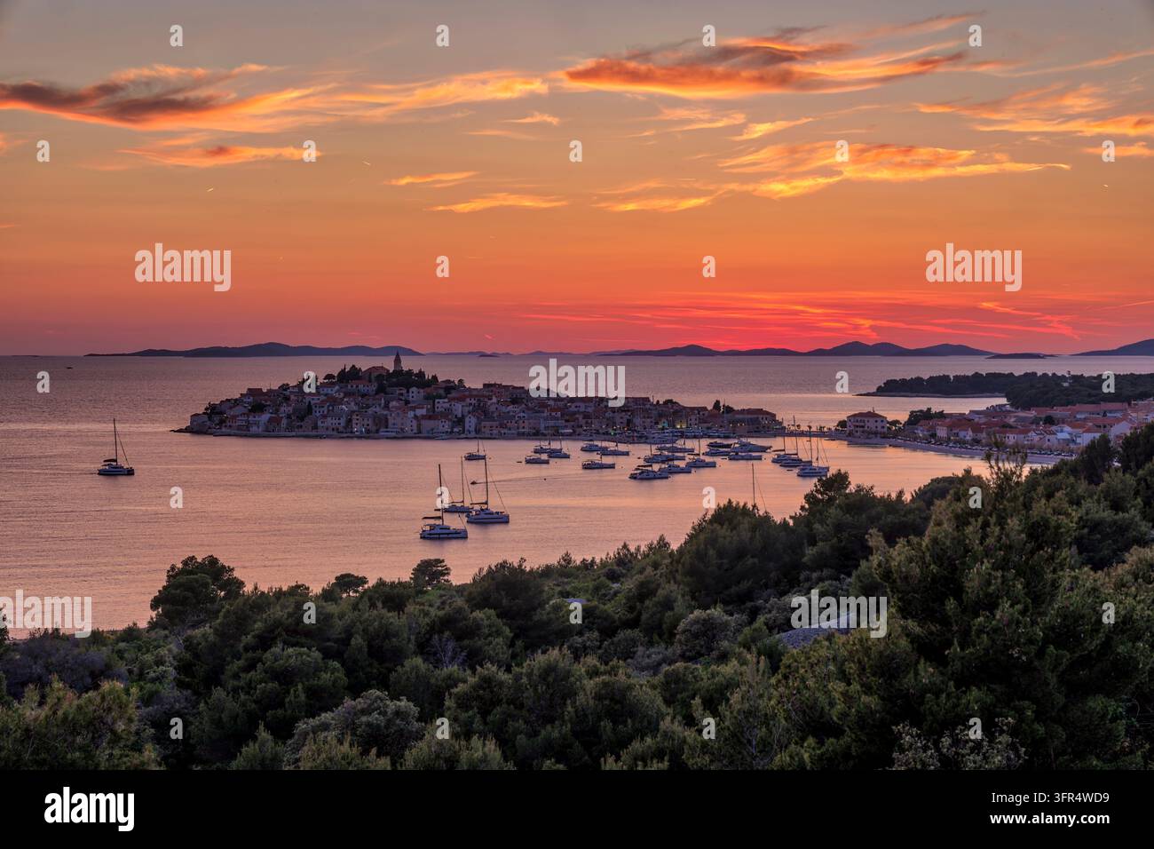 Vista ad angolo alto della penisola di Primošten circondata dal mare e da barche sotto un cielo crepuscolare luminoso. Foto Stock