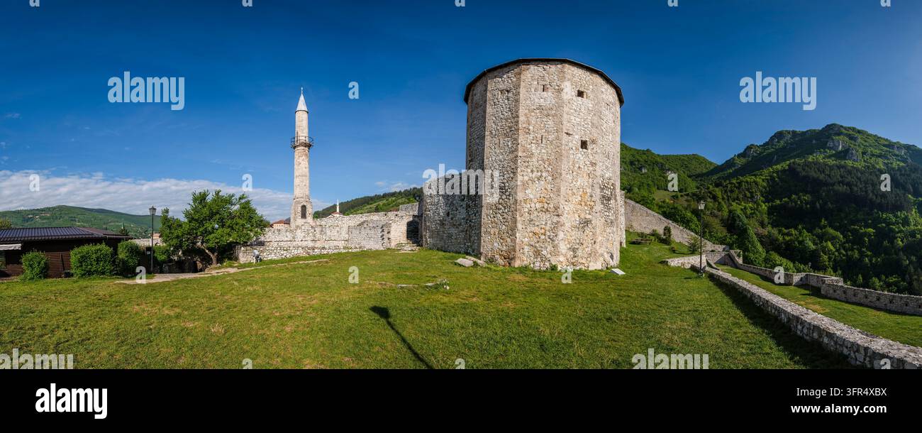 Vista panoramica sui prati del castello di Travnik, che mostra la sua grande torre circolare e il minareto lontano contro le colline verdi e lussureggianti oltre Foto Stock