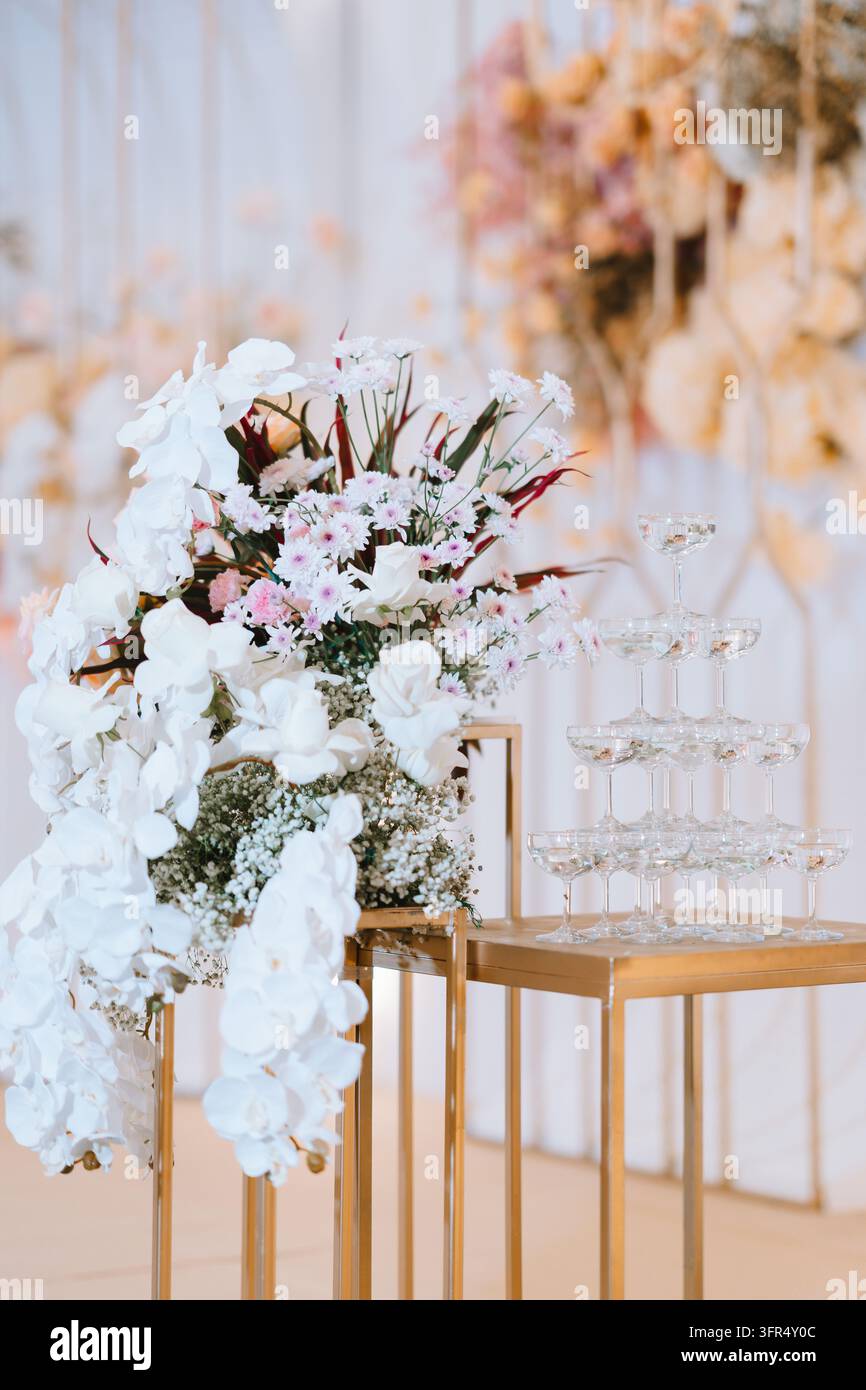 Ricevimento di matrimonio di lusso con una torre di champagne e uno splendido arrangiamento floreale bianco su supporti dorati Foto Stock
