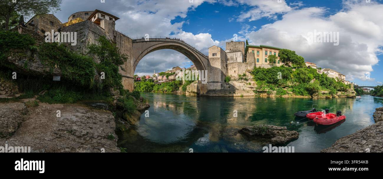 Vista panoramica sul fiume Neretva che mostra il Ponte Antico ricostruito dell'epoca ottomana a Mostar, con gli edifici storici in pietra circostanti. Mosta Foto Stock