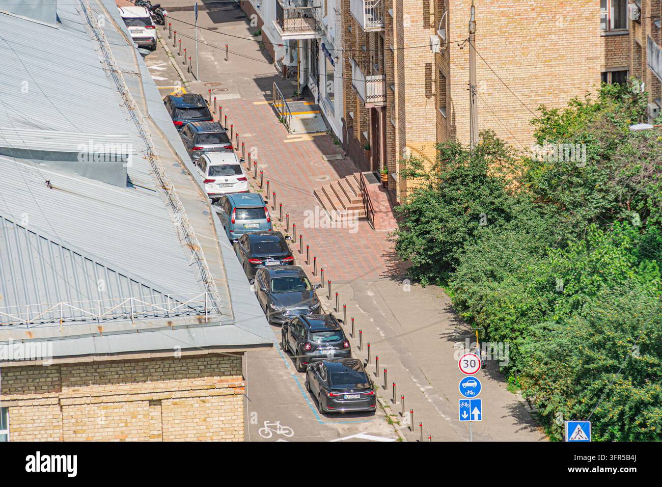 Vista aerea di una strada urbana funzionale a Kiev, Ucraina. Edifici dai toni della terra con finestre e porte fiancheggiano entrambi i lati. Auto parcheggiate a destra, blu b Foto Stock