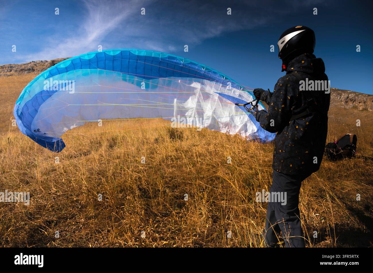 Un parapenditore atterra o si alza sull'erba gialla in una giornata di sole. Un uomo dopo o prima di un volo in parapendio. Planatore con paracadute, vista posteriore ad angolo ampio Foto Stock