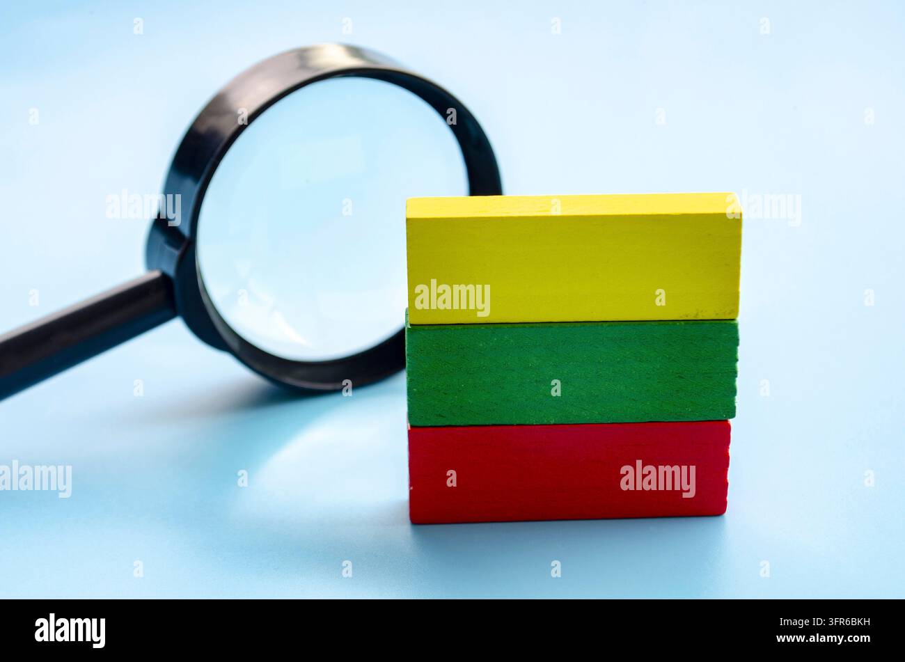 Blocchi di legno impilati colorati con una lente d'ingrandimento su una superficie di legno, che rappresentano l'apprendimento e la scoperta Foto Stock