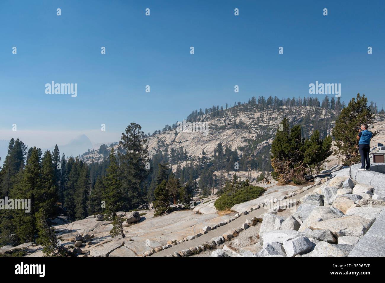 Turista a Olmsted point che fotografa Half Dome con il fumo dell'incendio boschivo del 2026 Dome Fire, Parco Nazionale di Yosemite, California, USA Foto Stock