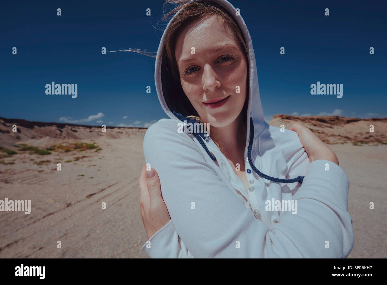 Grazioso ritratto di Frozen su una donna del vento che cammina in una felpa con cappuccio nel deserto Foto Stock