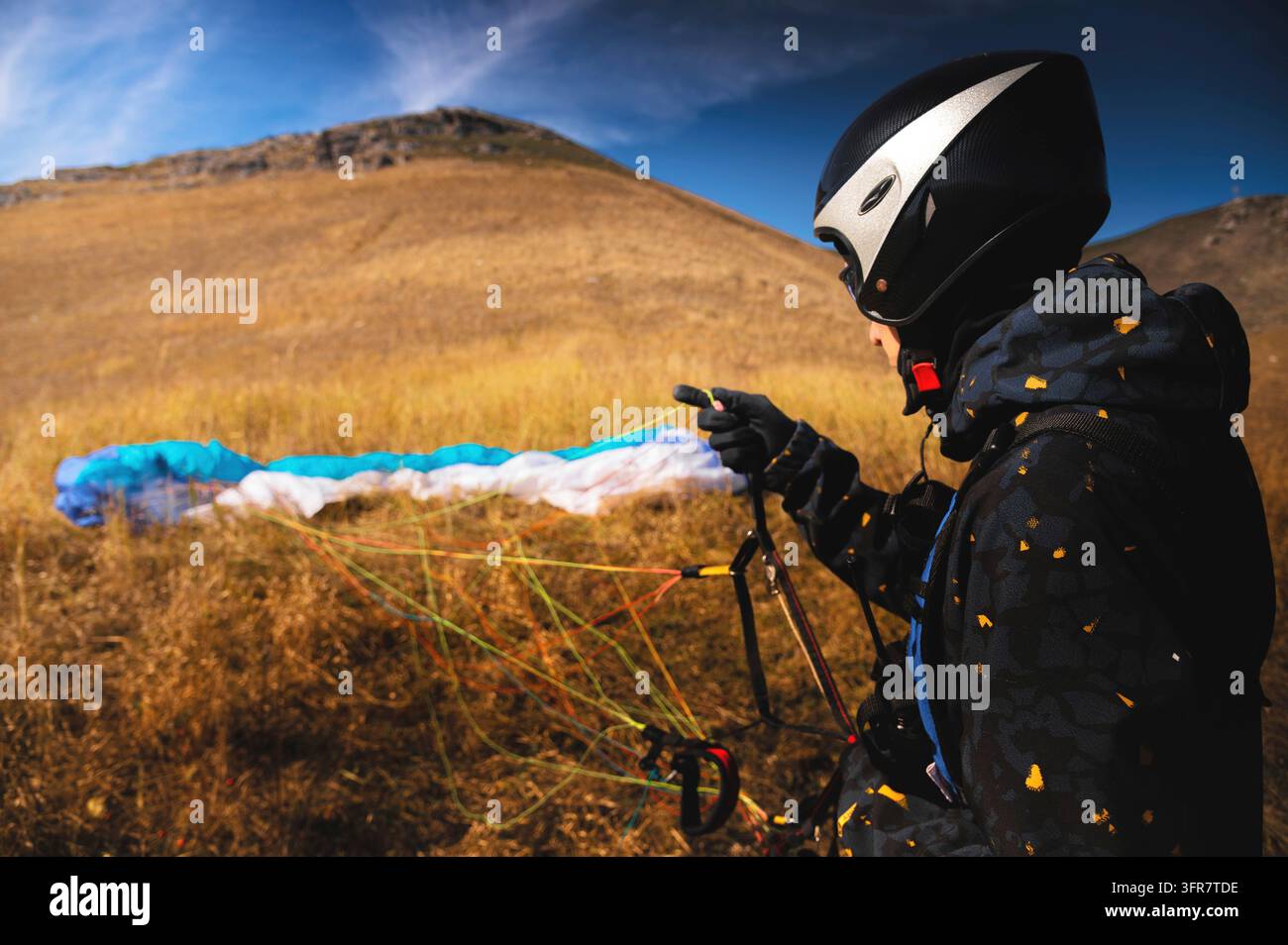 Un parapenditore atterra o si alza sull'erba gialla in una giornata di sole. Un uomo dopo o prima di un volo in parapendio. Planatore con paracadute, vista posteriore ad angolo ampio Foto Stock