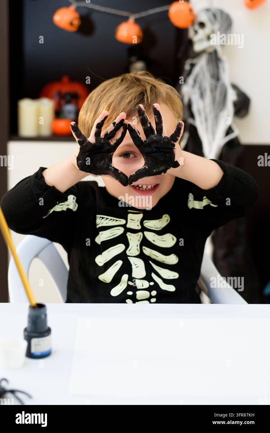 Un bambino vestito da scheletro mostra lavore di ragni e fantasmi. Festa di Halloween Foto Stock