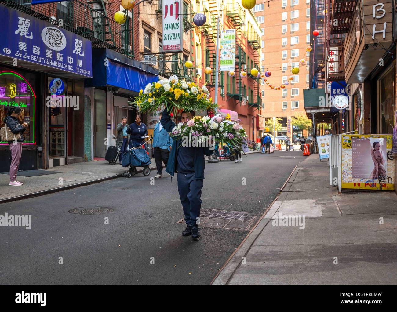 New York, NY, USA 11-09-2023 Un fattorino di fiori trasporta due grandi composizioni floreali lungo la strada a Chinatown con pedonale e via cittadina affollata Foto Stock