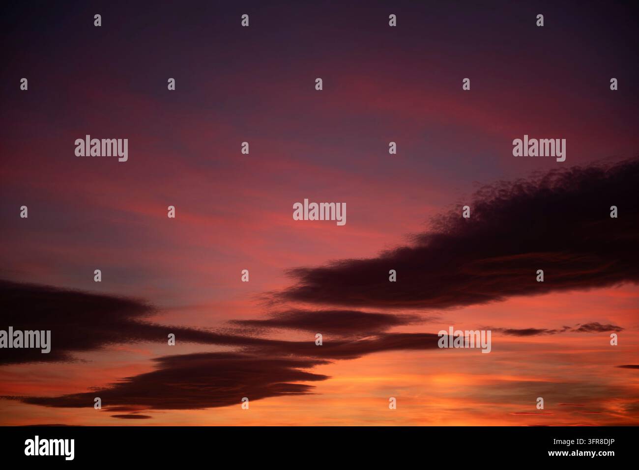 Un cielo infuocato al tramonto è illuminato da nuvole colorate in sfumature di arancione, giallo e magenta, creando uno spettacolo affascinante e che ispira stupore Foto Stock