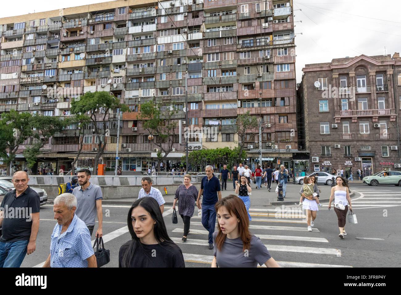 Folla di pedoni che attraversano una strada trafficata su un passaggio pedonale davanti ad edifici residenziali dell'era sovietica, Yerevan, Yerevan, Armenia Foto Stock