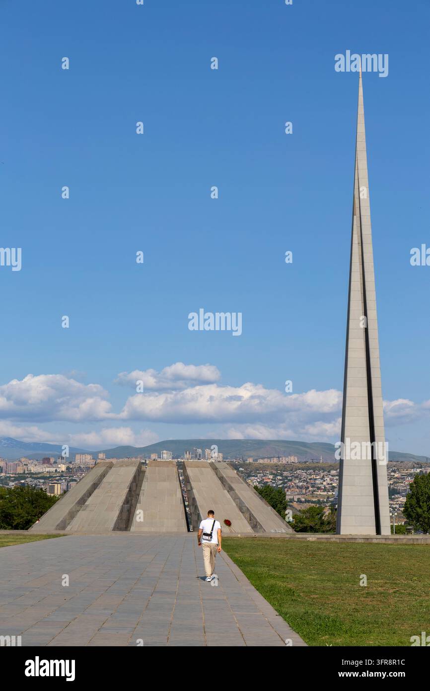 Uomo che cammina su un sentiero sotto l'alta guglia e la piramide a gradoni del complesso del Memoriale del Genocidio Armeno di Tsitsernakaberd, Yerevan, Armenia Foto Stock