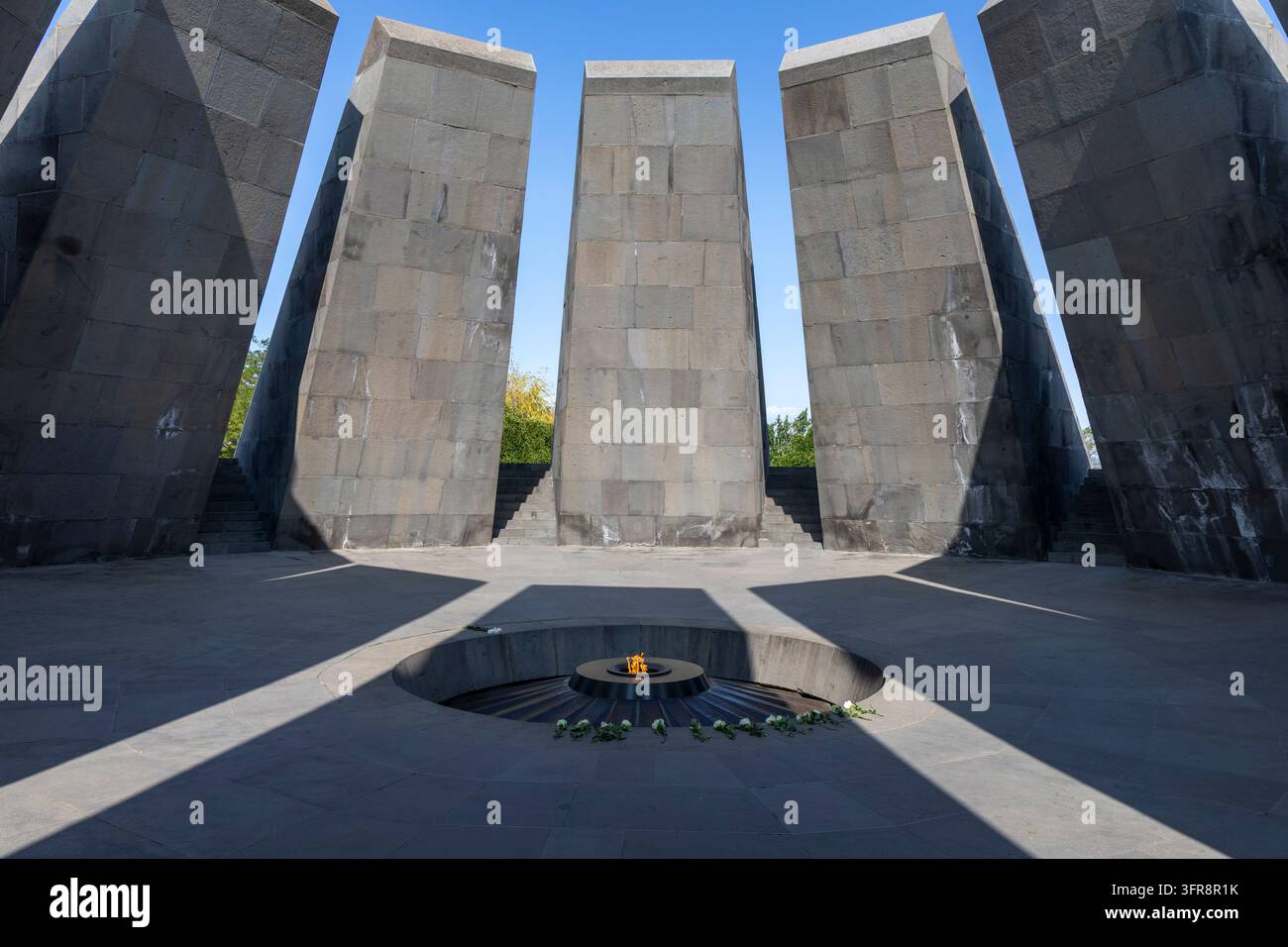 Visitatori che passeggiano vicino a una ghirlanda accanto alla struttura piramidale a gradini del complesso commemorativo del Genocidio Armeno di Tsitsernakaberd, a Yerevan, Armenia Foto Stock
