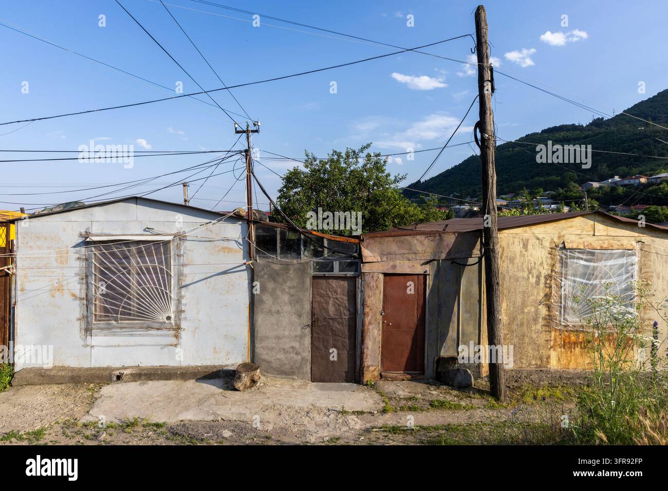 Filiera di vecchie capanne metalliche rustiche con porte arrugginite e linee elettriche, provincia di Syunik, Goris, Armenia Foto Stock