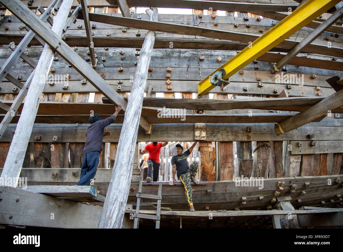 Un gruppo di costruttori navali lavora in alto su impalcature di legno all'interno della struttura di un grande dhow in costruzione, Gujarat, Mandvi, India Foto Stock