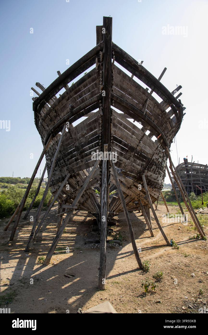 La prua in legno di un grande dhow è appoggiata su supporti di legno in un cantiere navale all'aperto, Gujarat, Mandvi, India Foto Stock