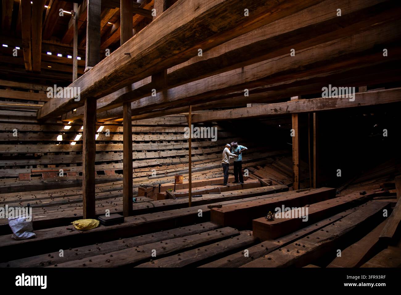 Due costruttori navali stanno insieme ispezionando le costole di legno all'interno dello scafo di una grande nave in costruzione in un cantiere navale a Mandvi, Gujarat, India Foto Stock