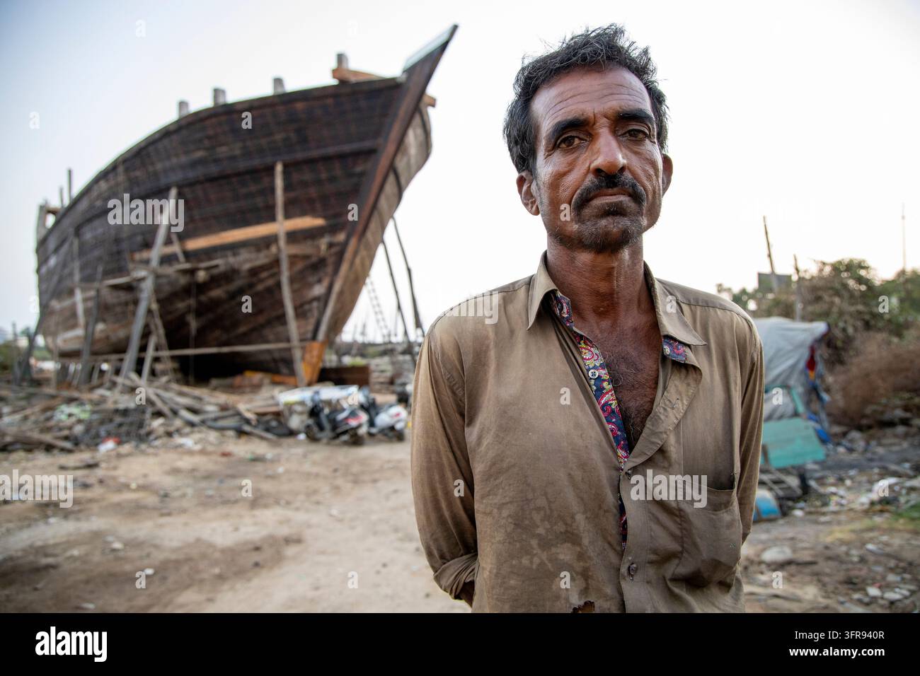 Un uomo si trova davanti allo scafo in legno di una nave in costruzione in un cantiere navale a Mandvi, Gujarat, India Foto Stock