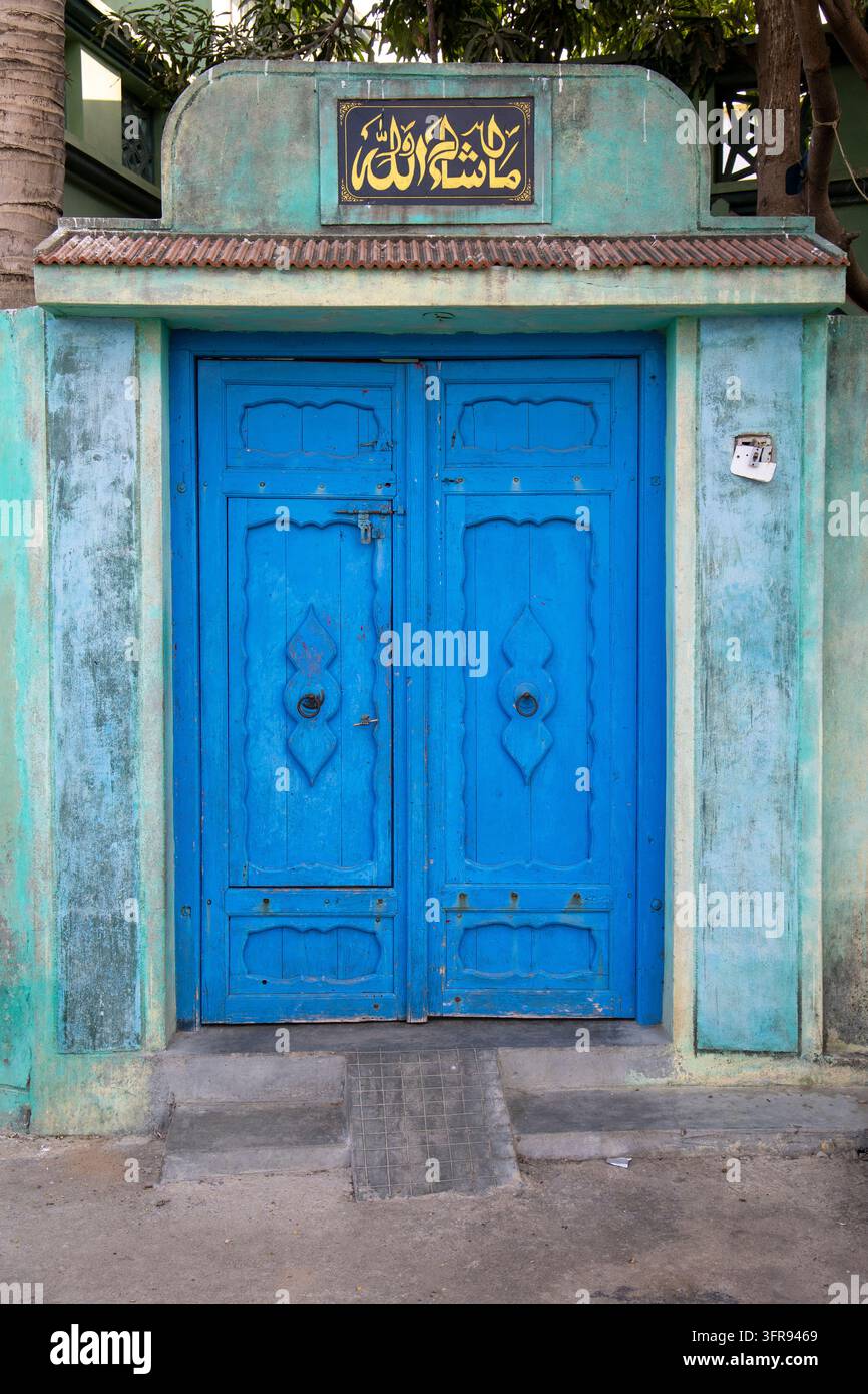 Doppia porta in legno blu con motivi intagliati posta sotto una targa murale con calligrafia araba, Gujarat, Mandvi, India Foto Stock