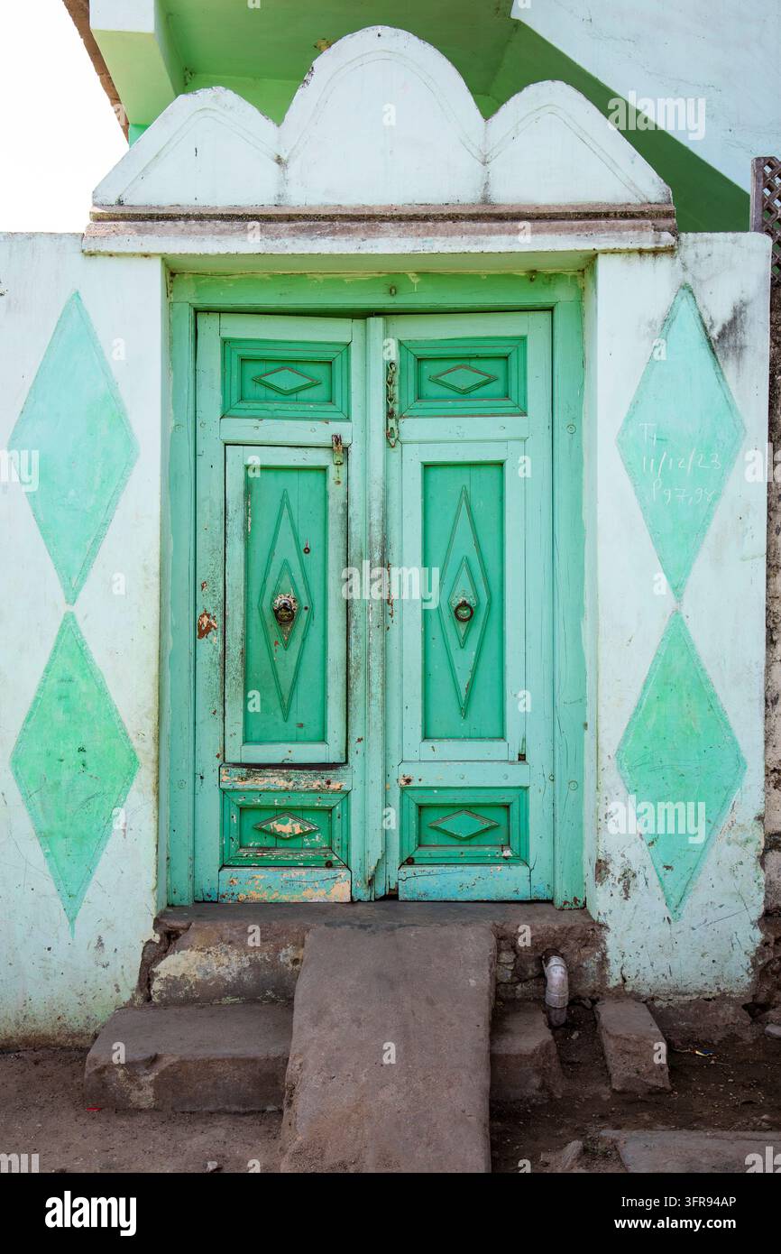 Una porta di legno consumata dipinta di verde menta si trova all'interno di un muro a motivi a diamante, Gujarat, Mandvi, India Foto Stock