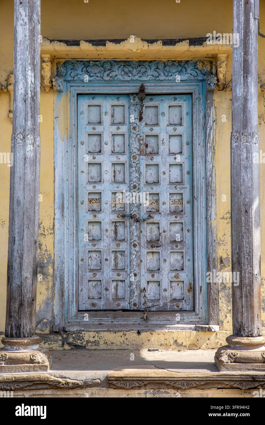 Una porta in legno intagliata è incorniciata da pilastri intagliati su una facciata gialla consumata, Gujarat, Mandvi, India Foto Stock