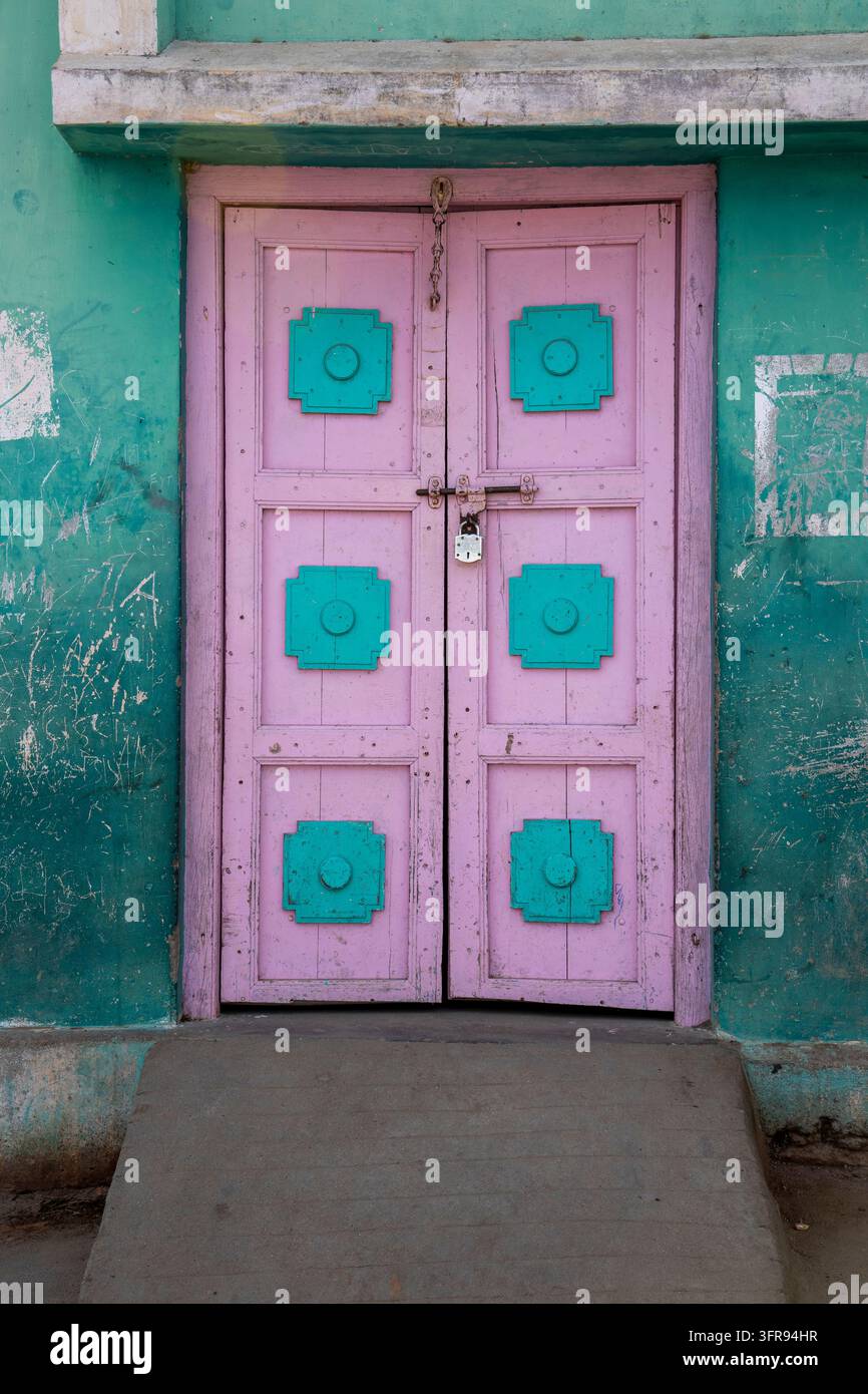Doppia porta in legno dipinta di rosa e turchese chiusa con un vecchio lucchetto, Gujarat, Mandvi, India Foto Stock