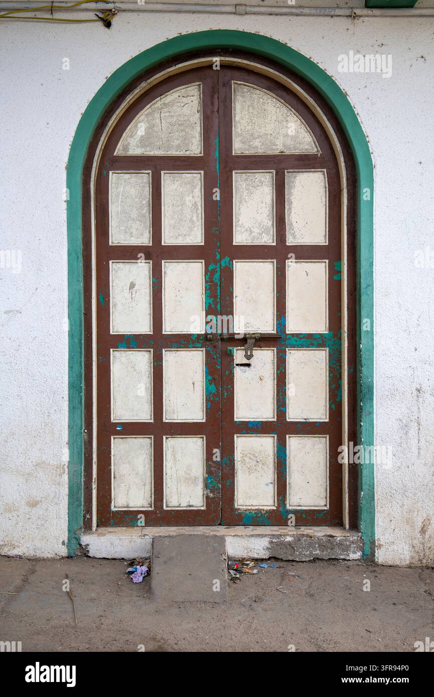 Doppia porta ad arco in legno marrone stagionato con infissi verdi e vernice scrostata, Gujarat, Mandvi, India Foto Stock