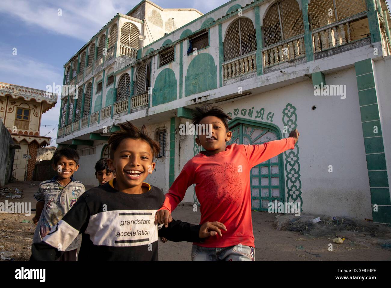 Ragazzi che ridono correndo e tenendosi per mano nella strada davanti a una vecchia haveli, Gujarat, Mandvi, India Foto Stock