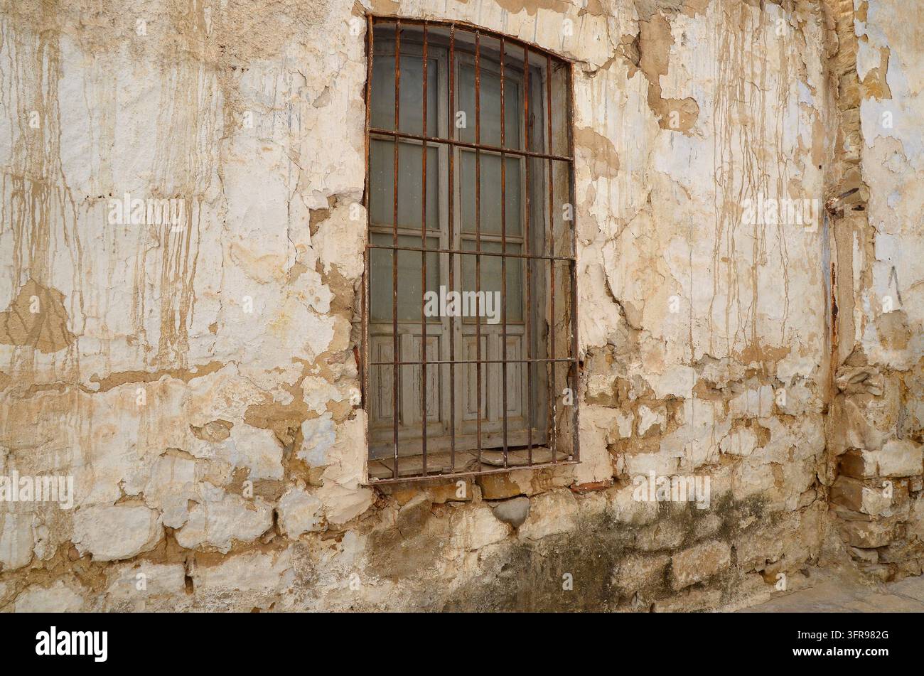 Dettaglio di una finestra rustica con una grata di ferro su una vecchia facciata in muratura, che mostra un grave degrado e distacco del malta. Úbeda, Andalusia, Spagna Foto Stock