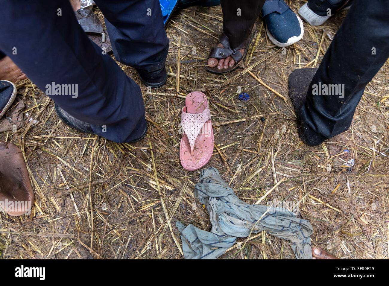 Piedi e sandali di pellegrini in piedi su un terreno di paglia con un sandalo rosa e un panno alla Maha Kumbh Mela, Uttar Pradesh, Prayagraj, India Foto Stock