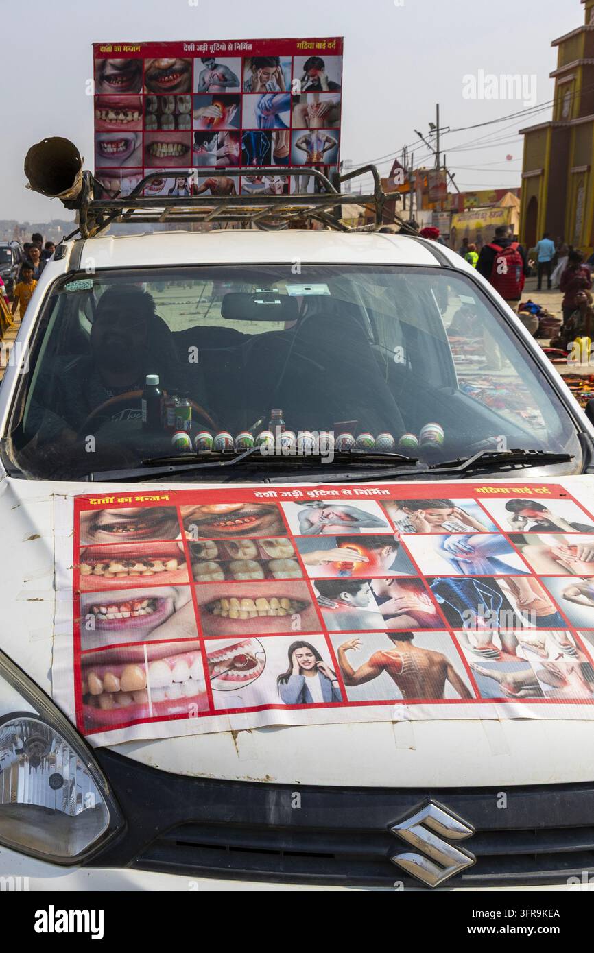 Auto bianca con un conducente e grandi poster di denti e rimedi per i dolori del corpo parcheggiata vicino alle bancarelle alla Maha Kumbh Mela, Uttar Pradesh, Prayagraj, India Foto Stock