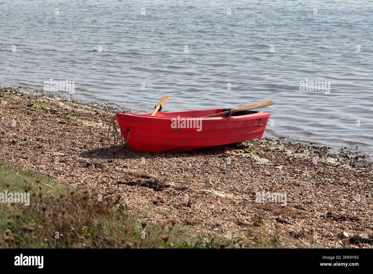 Una piccola barca a remi rossa trascinata su una spiaggia rocciosa Foto Stock