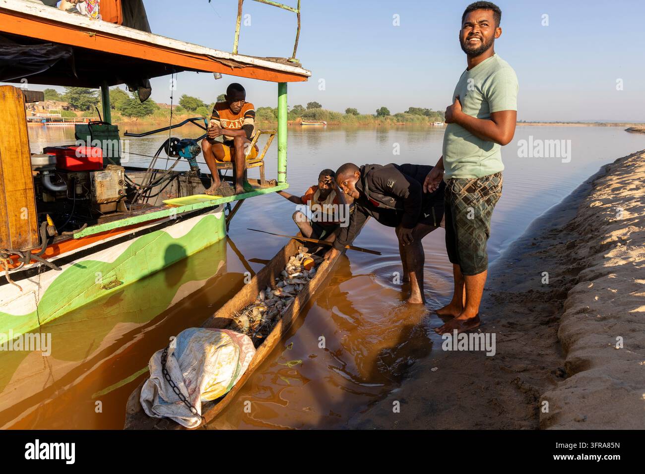 Pescatori che scaricano una canoa di tronchi piena di pesci accanto a una più grande imbarcazione fluviale sul fiume Tsiribihina, Menabe, Tsiribihina, Madagascar Foto Stock